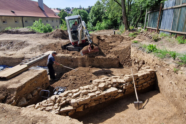 Postupné uvedení zkoumané plochy do původního stavu, zasypávání liniového hrobu č. 12 a 17 za průběžného utemování (zpevňování) zeminy. V popředí odhalen vnitřní líc kamenné tarasní zdi (foto Egon Ditmar, 26. 6. 2025).
